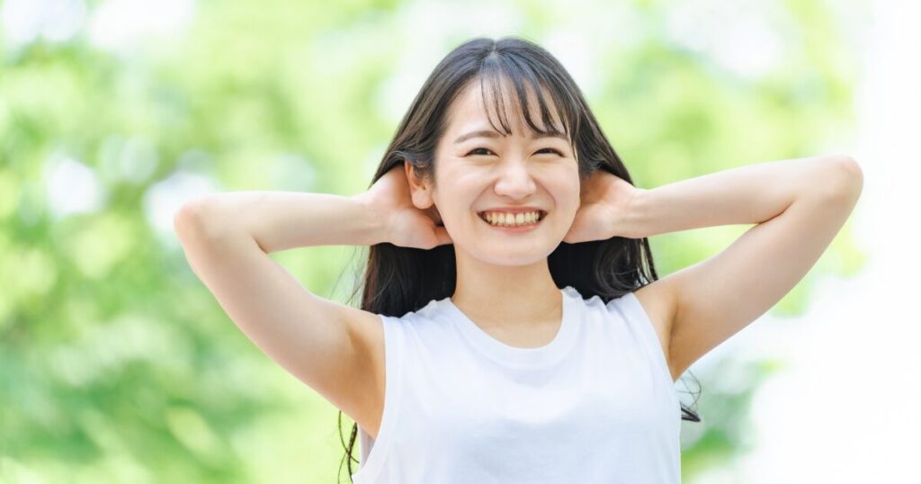 屋外で腕を後ろに回して笑顔の女性 リラックス 健康 美容