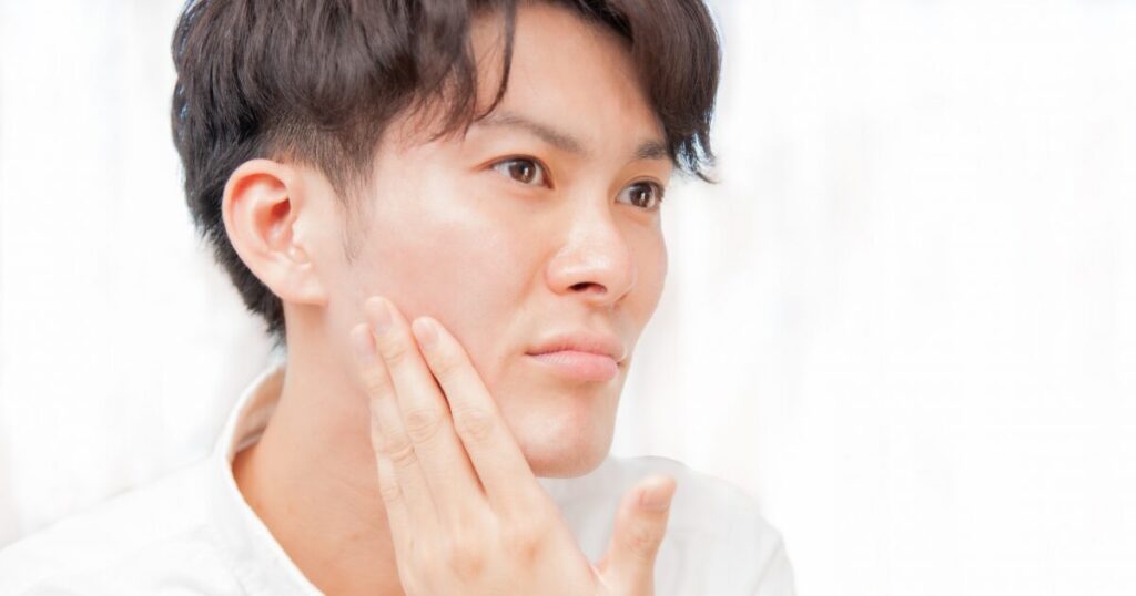 頬の肌状態を手で確認する男性のクローズアップ