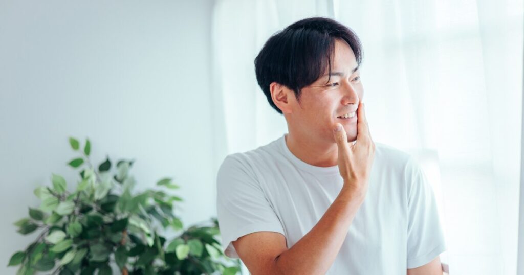自然光の部屋で頬を触りスキンケア効果を実感する男性