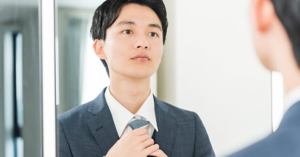 鏡の前で身だしなみを整えるスーツ姿の男性