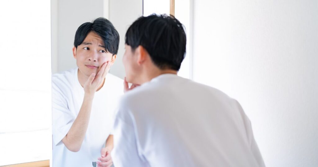 鏡を見て頬の肌状態を確認する男性